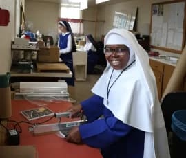 Sr. Maria Bosco shrink-wraps books while Sr. Phoebe works on packaging an order and Sr. Helen Marie prepares to print a mailing label.